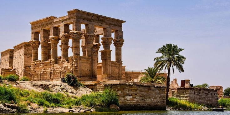 Antiker ägyptischer Tempel mit Säulen am Ufer des Nils, umgeben von Palmen und ruhigem Wasser