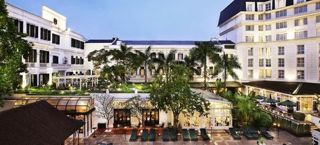 Weißes Hotel mit Bäumen im Vordergrund und leichter Beleuchtung 