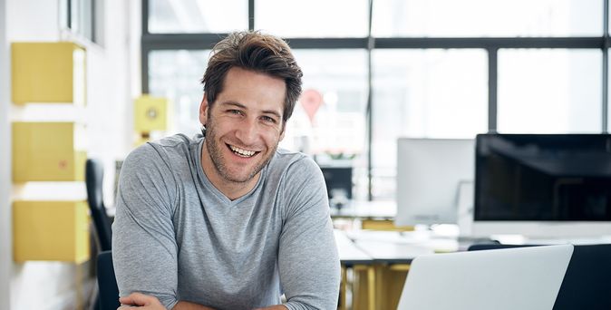 Mann vor mit Kaffeetasse vor Laptop in gelb dominiertem Büro