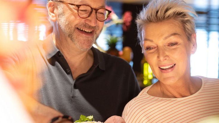 Ein lächelndes Paar steht gemeinsam an einem Buffet und stellt sich einen Teller mit frischen Speisen zusammen.