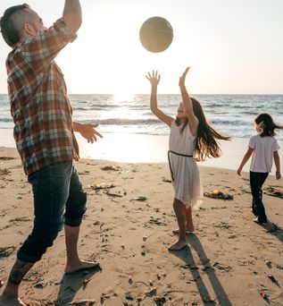 Familie spielt bei Sonnenuntergang Basketball am Strand