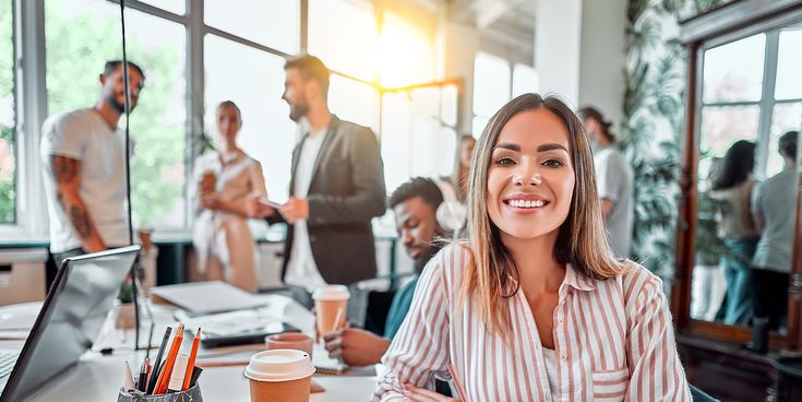 Lachende Frau im alternativen Büro mit Kaffeebecher und Kollegen