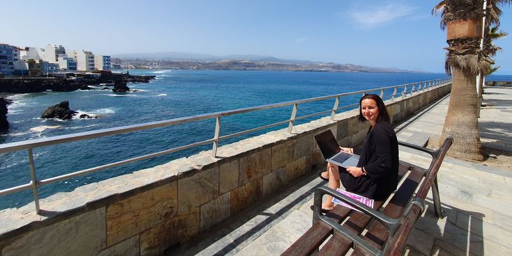 Autorin Sylvie Konzack sitzt mit Laptop an der Meerespromenade in Las Palmas auf Gran Canaria