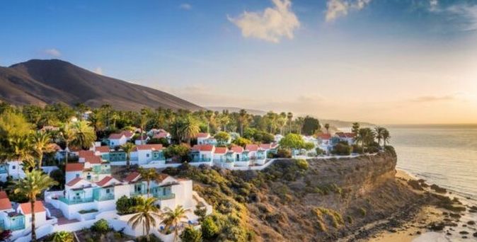 Küstenort mit weißen Häusern und roten Dächern auf einer Klippe mit Blick auf das Meer – mediterrane Urlaubsstimmung in der Abendsonne.