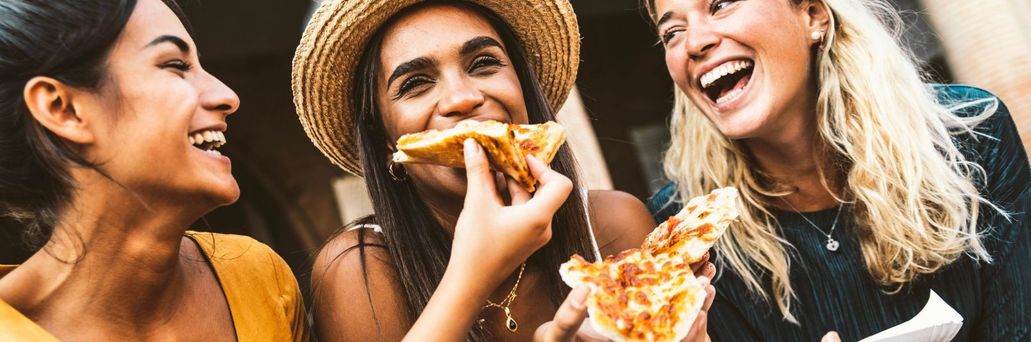 Drei Freundinnen lachen gemeinsam und essen Pizza in der Stadt