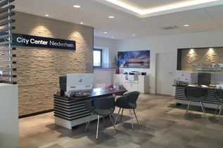 Innenansicht des Reisebüros City Center Niederrhein mit modernen Beratungsplätzen, Steinwand und Urlaubsbild an der Wand.