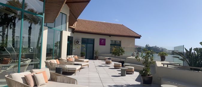 Sonnige Spa-Terrasse mit hellen Loungemöbeln, Pflanzen und weitem Blick über die Hotelanlage.