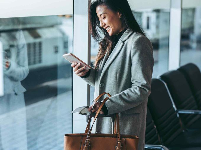 Geschäftsreisende lächelt auf ihr Smartphone im Flughafen-Wartebereich.
