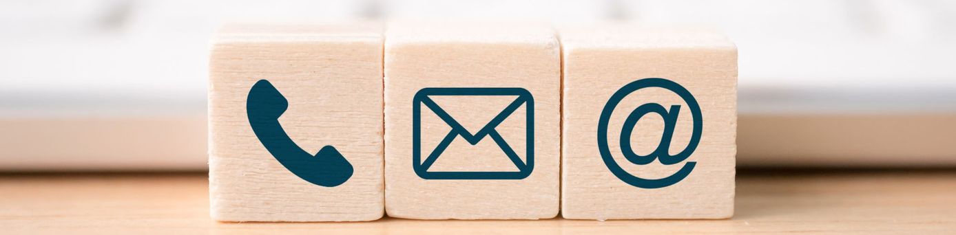 Drei Holzblöcke mit Symbolen für Telefon, E-Mail und Internetadresse vor einer Tastatur – Darstellung moderner Kontaktmöglichkeiten.