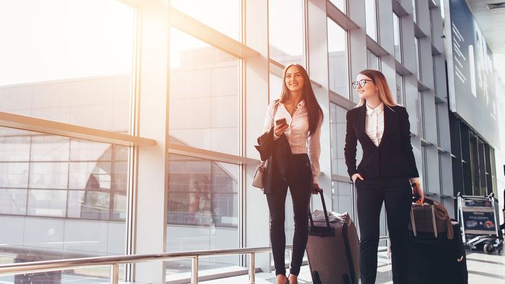 Geschäftsfrauen mit Trolleys an Flughafen-Fensterfront