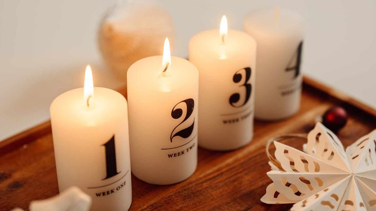 Vier brennende Adventskerzen mit den Zahlen eins bis vier stehen auf einem Holztablett und symbolisieren die besinnliche Vorweihnachtszeit.
