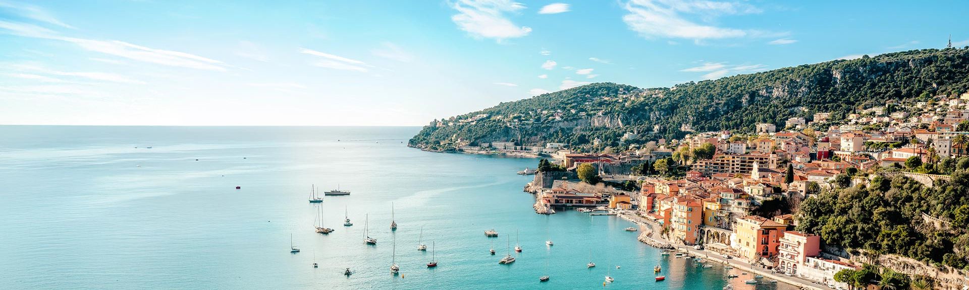 Panorama einer ruhigen Küstenstadt mit kleinen Booten auf glattem Meer unter klarem Himmel.