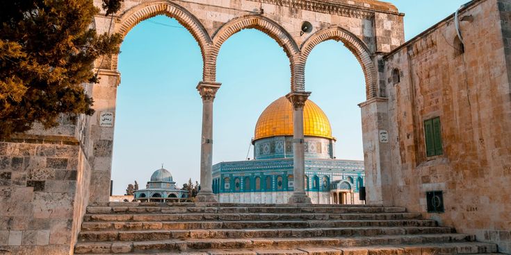 Der Felsendom in Jerusalem mit goldener Kuppel, gesehen durch alte Steinbögen bei klarem Himmel.