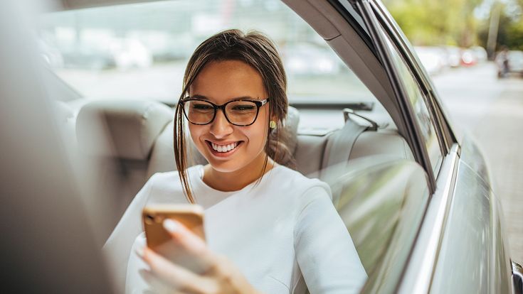 Frau mit Handy sitzt hinten im Auto