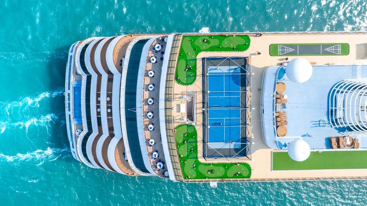 Luftaufnahme eines Hochseekreuzfahrtschiffs mit Sonnendeck, Pool und Freizeitbereichen – moderner Luxus auf dem offenen Meer mit Blick auf türkisfarbenes Wasser.