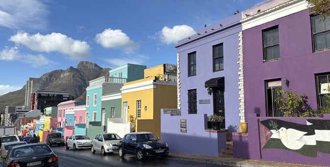 Farbenfrohe Häuser in Lila, Türkis, Gelb und Rosa an einer Straße im Bo-Kaap mit dem Tafelberg im Hintergrund.