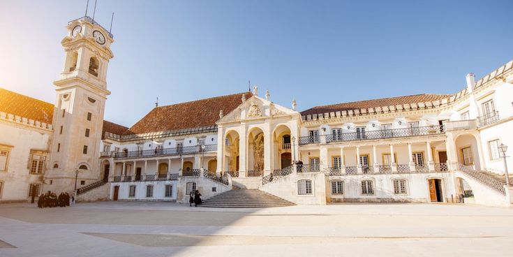Historischer Innenhof der Universität Coimbra mit weißer Fassade, breiter Freitreppe und Uhrturm.