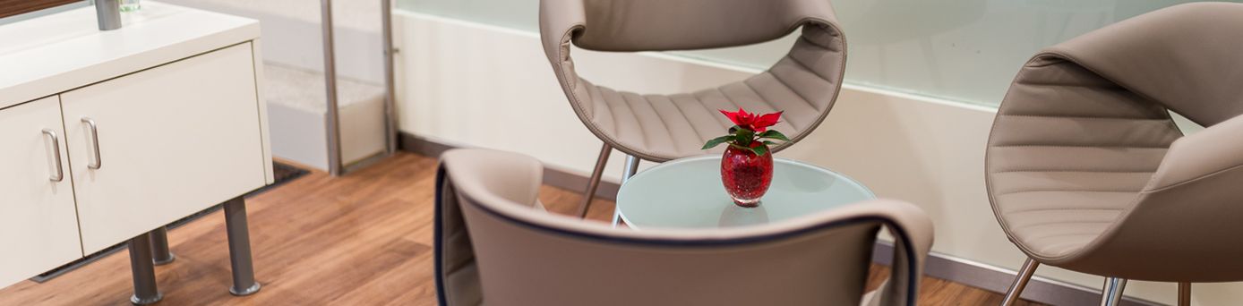 Moderner Wartebereich mit Designstühlen und kleinem Glastisch, auf dem eine rote Vase mit Blume steht – einladende Atmosphäre in einem Reisebüro.
