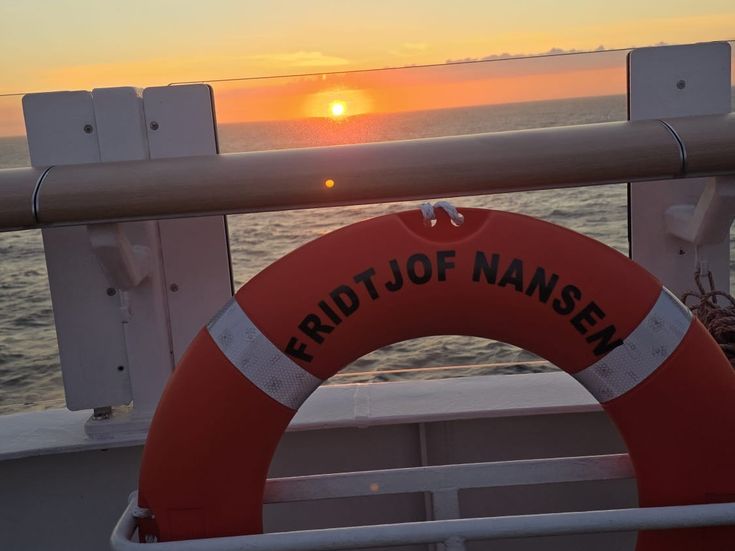 Sonnenuntergang über dem Meer, aufgenommen vom Deck der Fähre „Fridtjof Nansen“, mit rotem Rettungsring im Vordergrund.