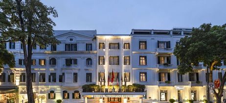 Weißes Hotel mit Bäumen im Vordergrund und leichter Beleuchtung 
