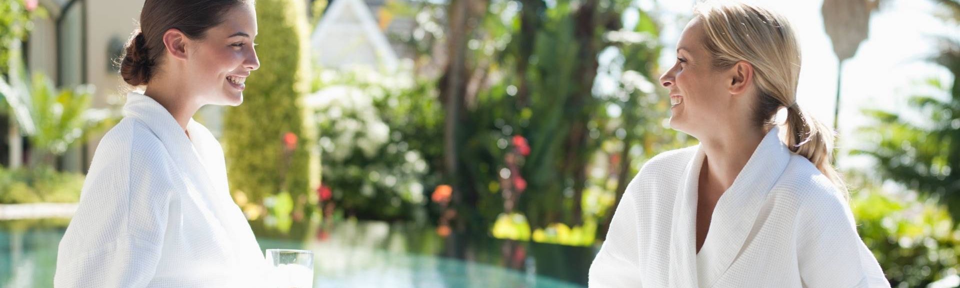 Freundinnen im Gespräch am Pool im Bademantel