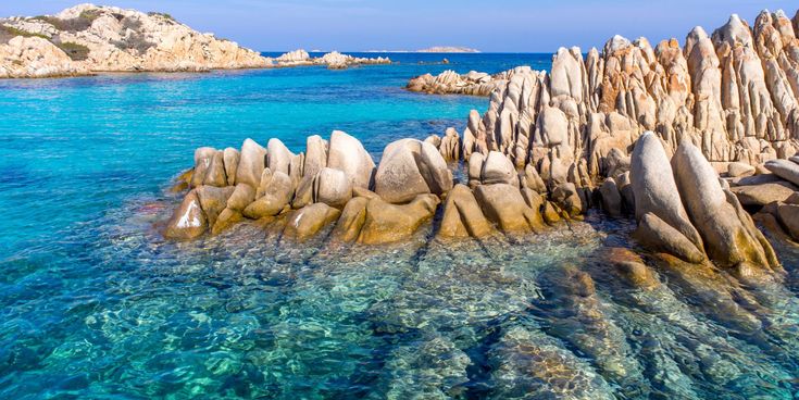 Kristallklares Wasser und markante Granitfelsen an der Costa Smeralda auf Sardinien, Italien, unter blauem Himmel.