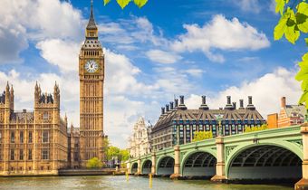Big Ben und die Westminster Bridge in London am Ufer der Themse unter blauem Himmel mit weißen Wolken.