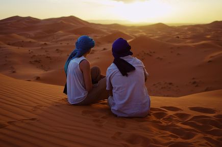 Menschen sitzen bei Sonnenuntergang auf Sanddüne in Wüste in Merzouga