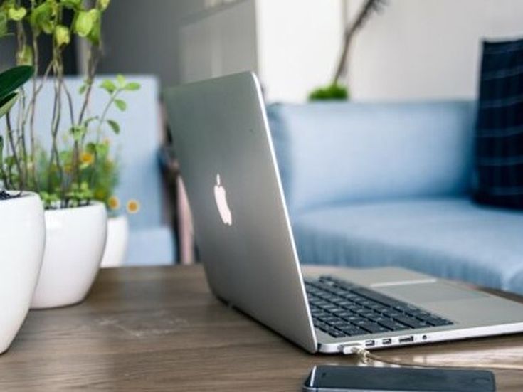 Offenes Laptop auf einem Holztisch neben grünen Pflanzen und Smartphone – moderne, ruhige Arbeitsatmosphäre im Büro oder Homeoffice.