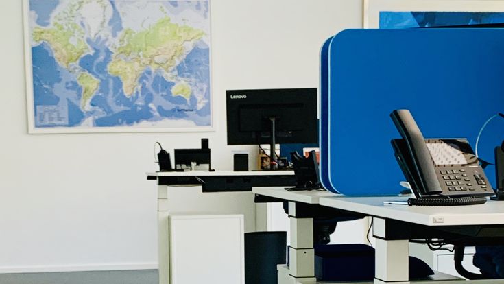 Modernes Büro mit höhenverstellbaren Schreibtischen, Monitoren und einer Weltkarte an der Wand.