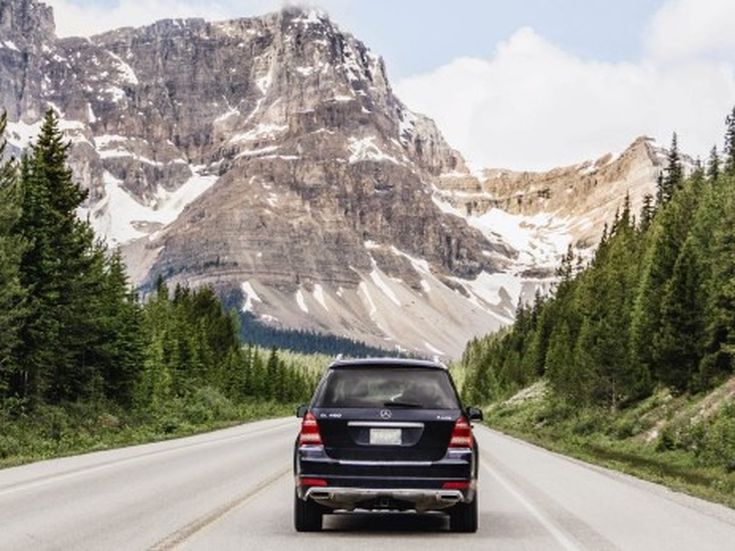 Auto fährt auf einsamer Bergstraße in Richtung schneebedeckter Gipfel – Gefühl von Freiheit und Abenteuer.