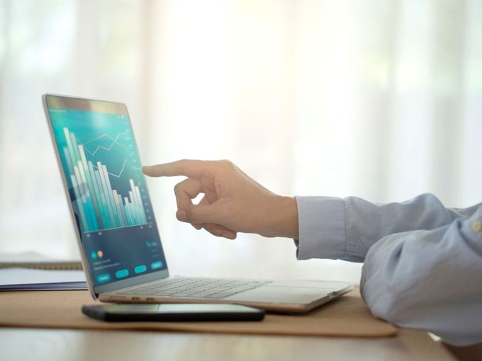 Männerhand deutet auf einen Laptop-Bildschirm, der ein Chart mit Balkendiagrammen zeigt