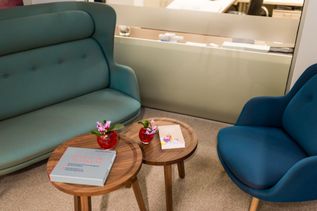 Gemütlicher Sitzbereich mit blauem Sofa und Sessel, zwei kleinen Holztischen, Blumenvasen und Reiselektüre.