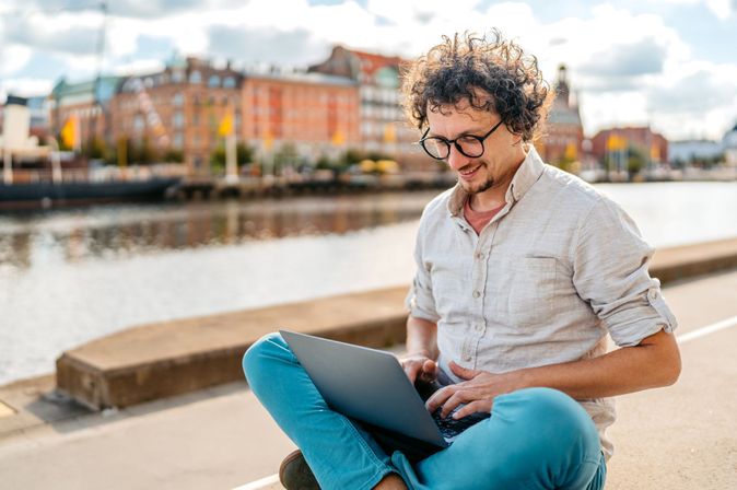 Mann mit Laptop am Kai vor der Stadtkulisse von Malmö in Schweden