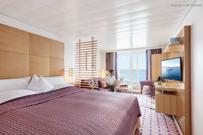 Bett, TV und sitzender Gast in Kabine vom Schiff MS Europa 2 der Reederei Hapag Lloyd Cruises