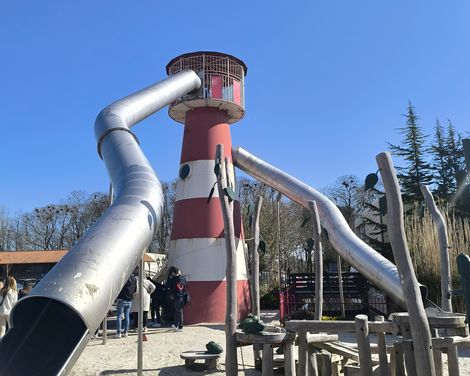 Spielplatz mit einer Rutsche, die aus einem Leuchtturm startet