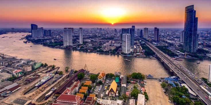 Blick über Bangkok bei Sonnenuntergang mit dem Chao-Phraya-Fluss, modernen Hochhäusern und traditionellen Tempeldächern – Verbindung von Kultur, Moderne und pulsierendem Stadtleben in Thailands Hauptstadt.