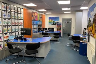 Innenansicht eines Reisebüros mit mehreren Beratungsplätzen, blauen Schreibtischen und Prospektwand.