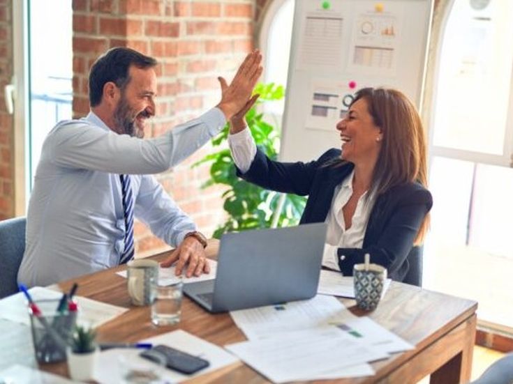 Zwei Kollegen freuen sich über ein erfolgreiches Meeting und geben sich ein High Five im Büro.