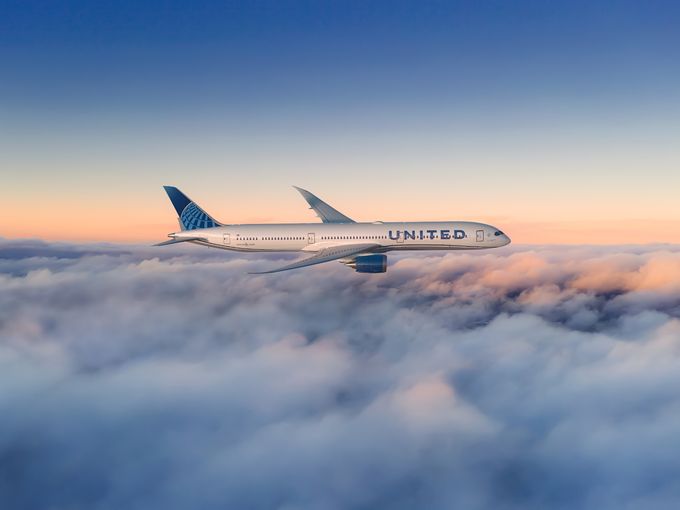 United Airlines Boeing 787 Dreamliner im Seitenprofil über einer Wolkendecke, im Hintergrund ein Sonnenuntergangshimmel.
