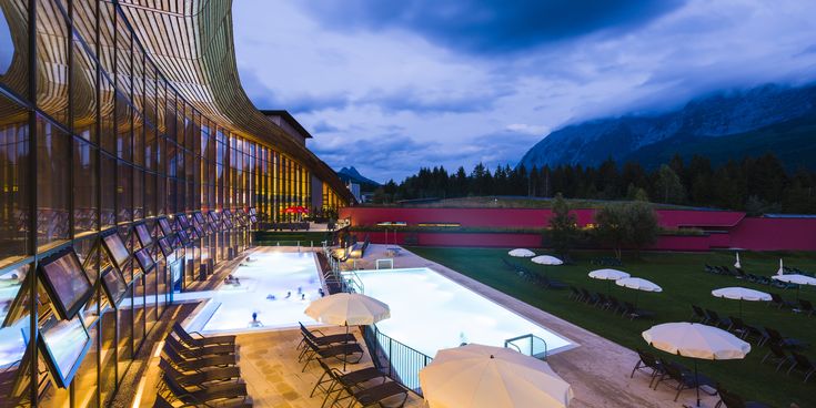 Abendstimmung im Aldiana Club Salzkammergut mit beleuchtetem Außenpool, moderner Glasarchitektur und Blick auf die umliegende Berglandschaft – Symbol für Wellness, Natur und Entspannung in den Alpen.