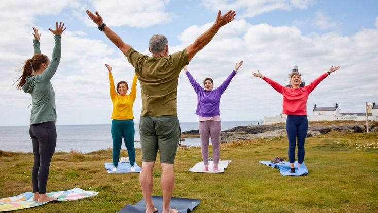 Gruppe von Menschen macht Yoga oder Dehnübungen im Freien mit Meerblick.