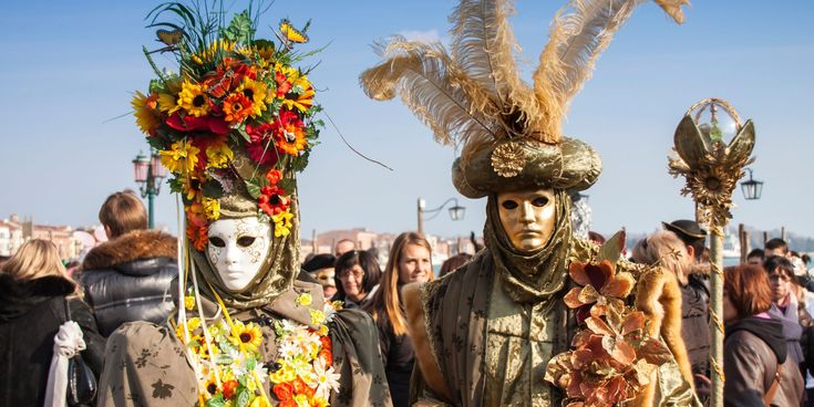 Zwei Personen in aufwendig gestalteten Masken und Kostümen beim Karneval in Venedig vor einer Menschenmenge