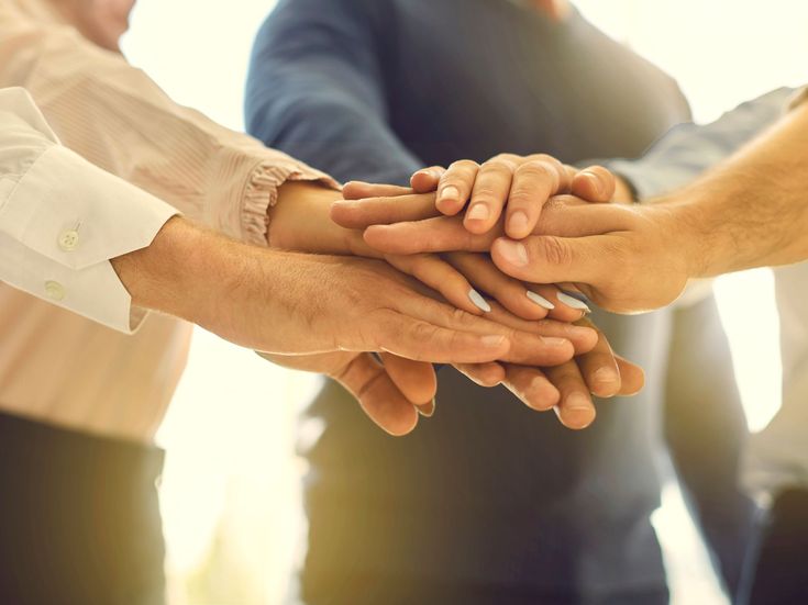 Mehrere Menschen legen ihre Hände übereinander – Symbol für Teamgeist, Zusammenhalt und gemeinsames Engagement im Unternehmen.