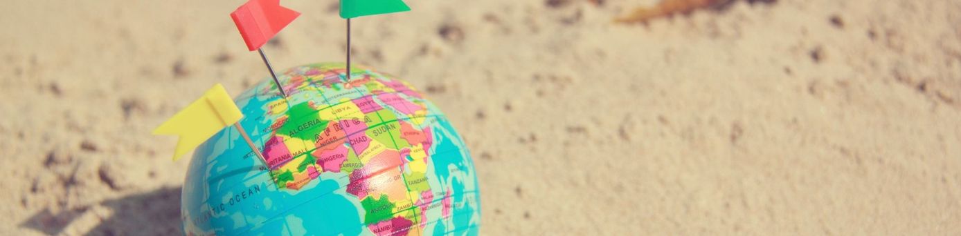 Zwei Personen planen eine Reise mit einer Weltkarte auf dem Tisch, umgeben von Reisefotos, einer Kamera, einer Tasse Kaffee und einem Modellflugzeug – Symbol für Reiselust und Urlaubsplanung.