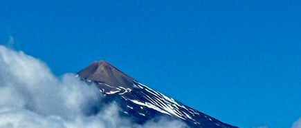 Schneebedeckter Gipfel des Teide ragt zwischen weißen Wolken in den tiefblauen Himmel.