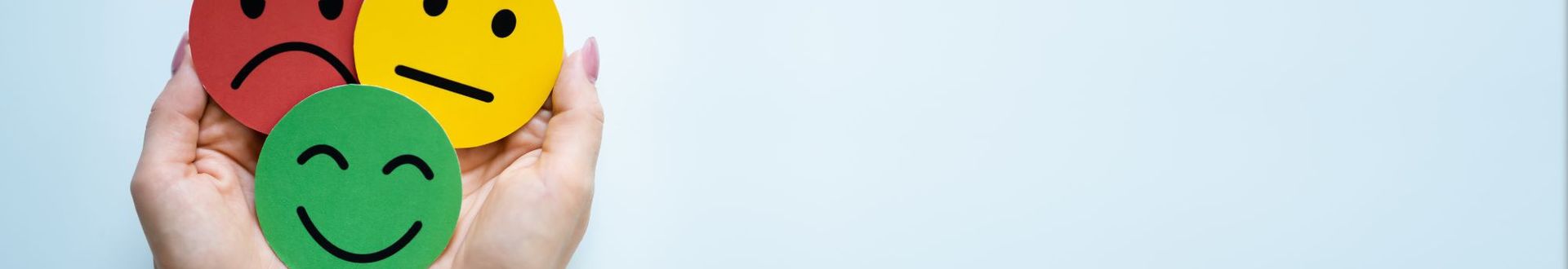 Zwei Hände halten drei runde Karten mit Smileys in Grün, Gelb und Rot, die unterschiedliche Stimmungen und Kundenfeedback symbolisieren.