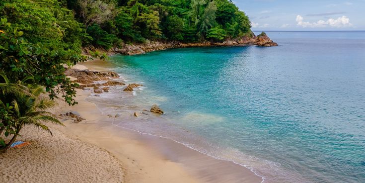 Tropischer Sandstrand mit türkisblauem Wasser und üppiger grüner Vegetation am Banana Beach auf Phuket, Thailand.