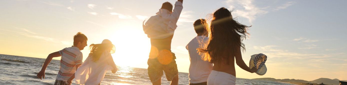 Gruppe junger Menschen läuft lachend bei Sonnenuntergang am Strand entlang – Sinnbild für gemeinsames Reisen, Abenteuerlust und Bildungsreisen mit Erlebnischarakter.