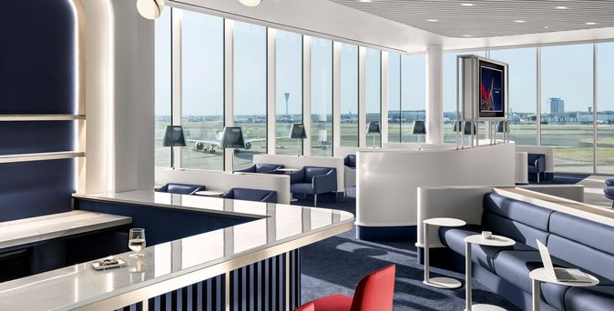 Air France Lounge in London Heathrow mit marmorner Bar, roten Stühlen, blauen Loungesofas und großen Fenstern mit Blick aufs Rollfeld.